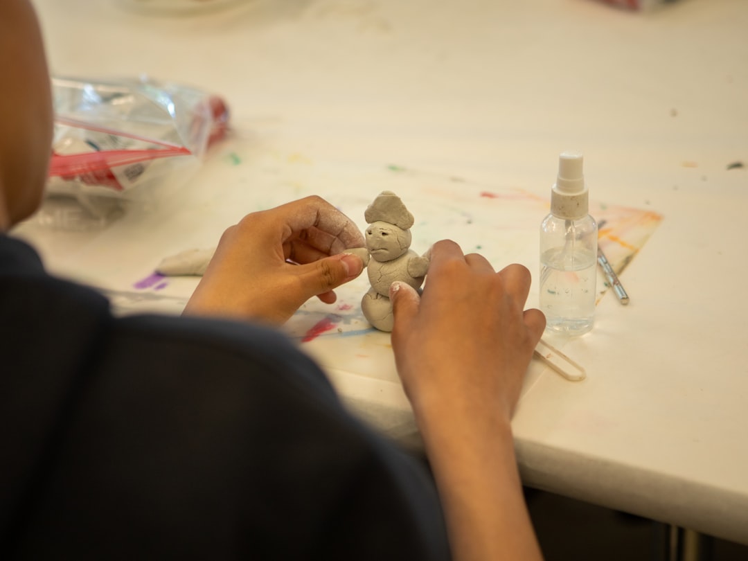 Mão pintando detalhes de uma peça pequena de cerâmica fria com pincel fino